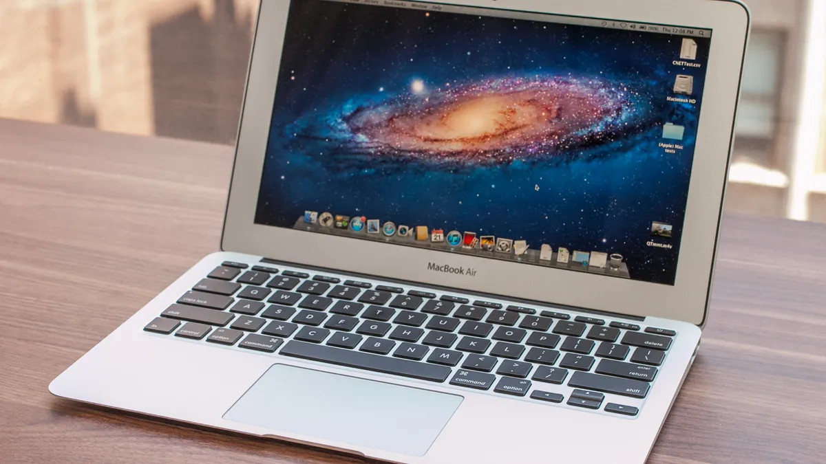 A MacBook Air is open on a wooden surface, displaying a desktop with a galaxy-themed wallpaper.